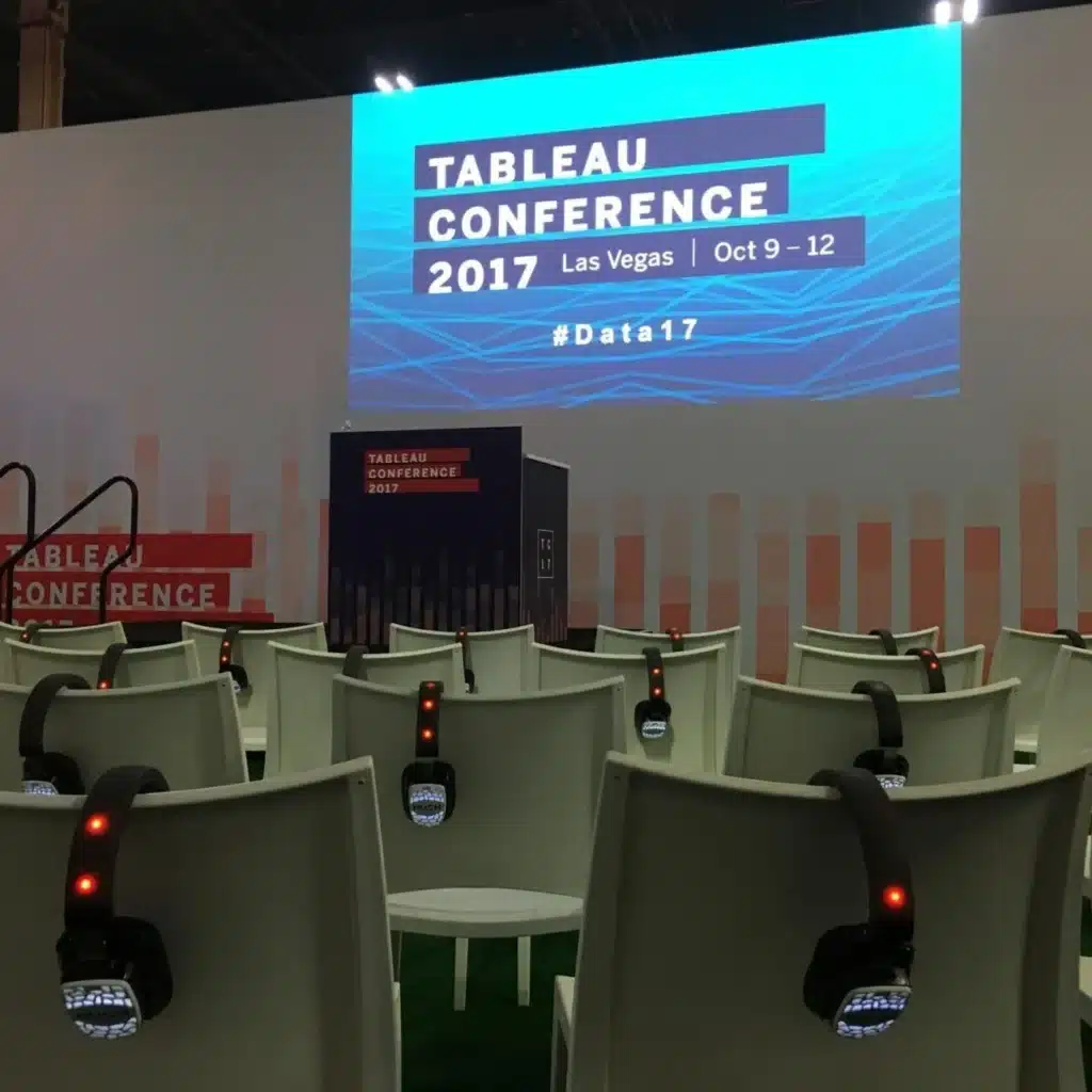 Rows of white chairs with headphones are set up facing a large screen displaying "Tableau Conference 2017, Las Vegas, Oct 9–12, #Data17," breaking language barriers with silent conferences in a modern venue.